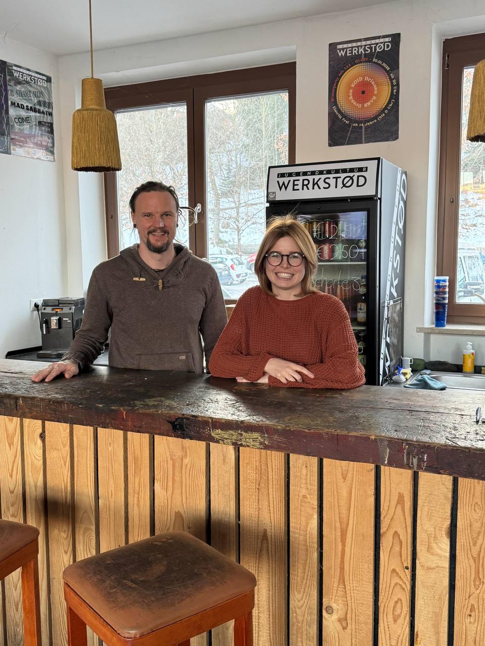 Hinter einer Bar stehen Marco Lorenz und Marlene Schönberger und lächeln in die Kamera.